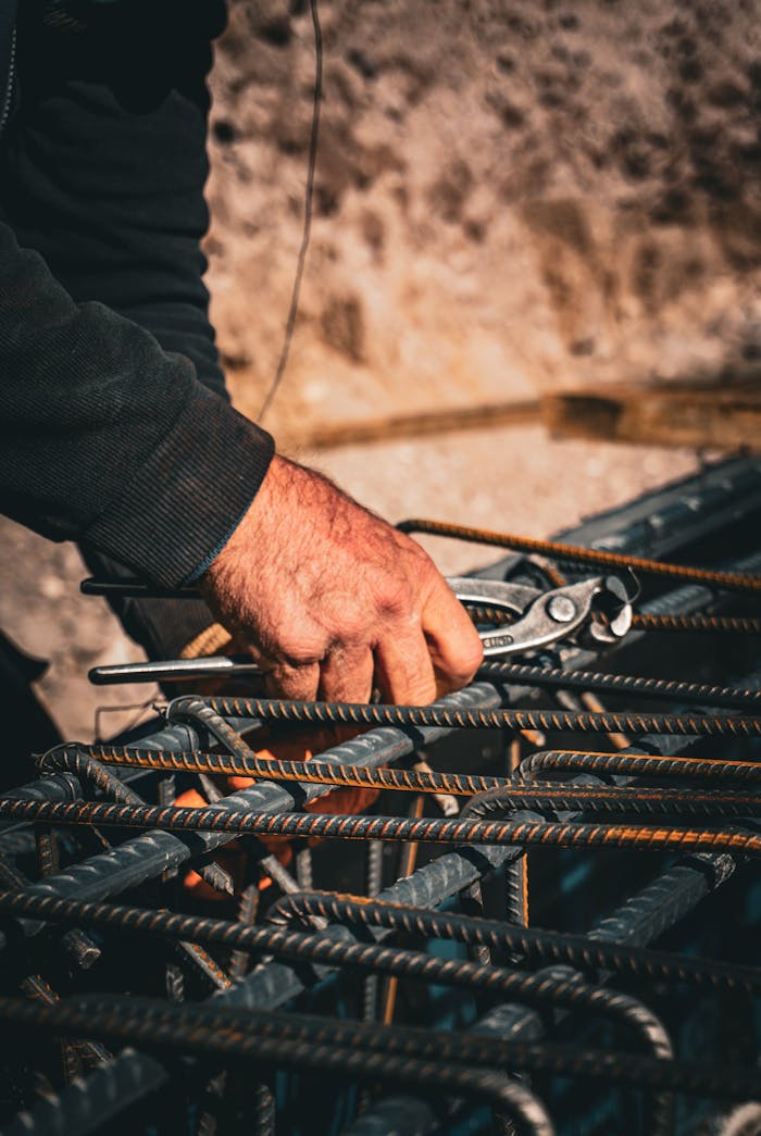 Close-up of a workers hand using a tool to handle rebar at a construction site, showcasing rugged labor.
