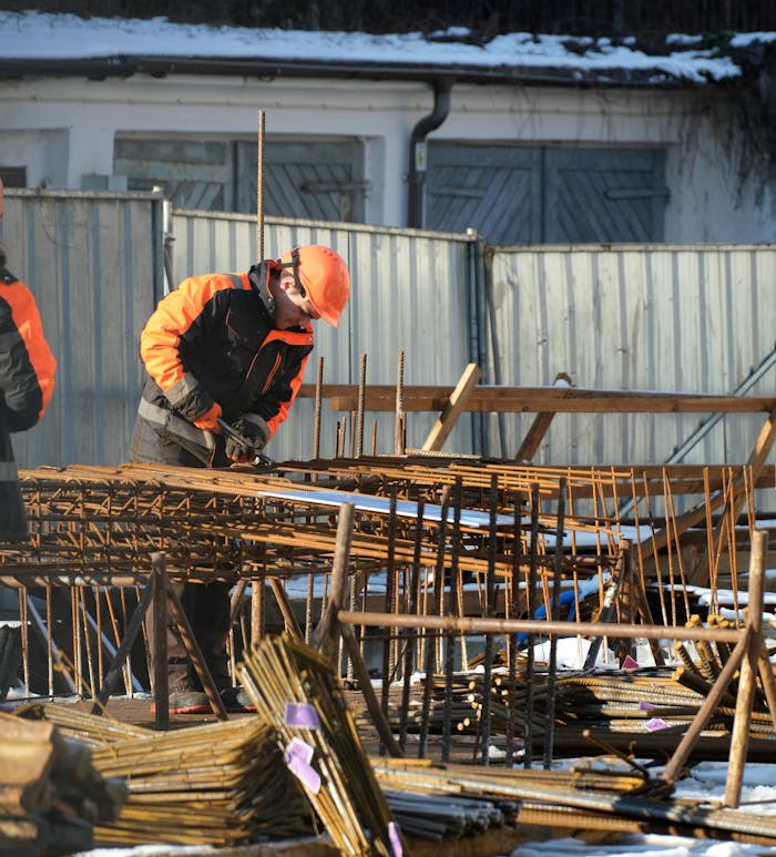 Workers in protective gear handling rebar at snowy construction site in Gdańsk.